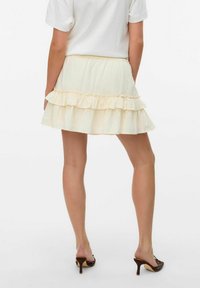 Jupe tiered plissée jaune clair avec une taille élastique. Fabriquée en tissu texturé. Associée à des mules à talons hauts marron.