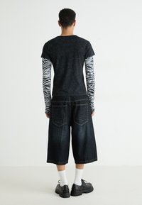 Camiseta negra de manga corta sobre una camisa de manga larga con rayas de cebra, combinada con culottes de mezclilla oscuros y zapatos de plataforma negros con tachuelas.