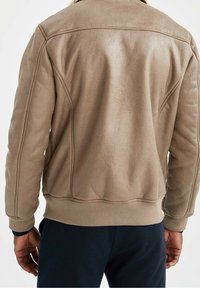 Veste en tissu brun texturé avec ourlet et poignets côtelés, présentant des coutures discrètes et un col ; conçue pour une coupe décontractée.