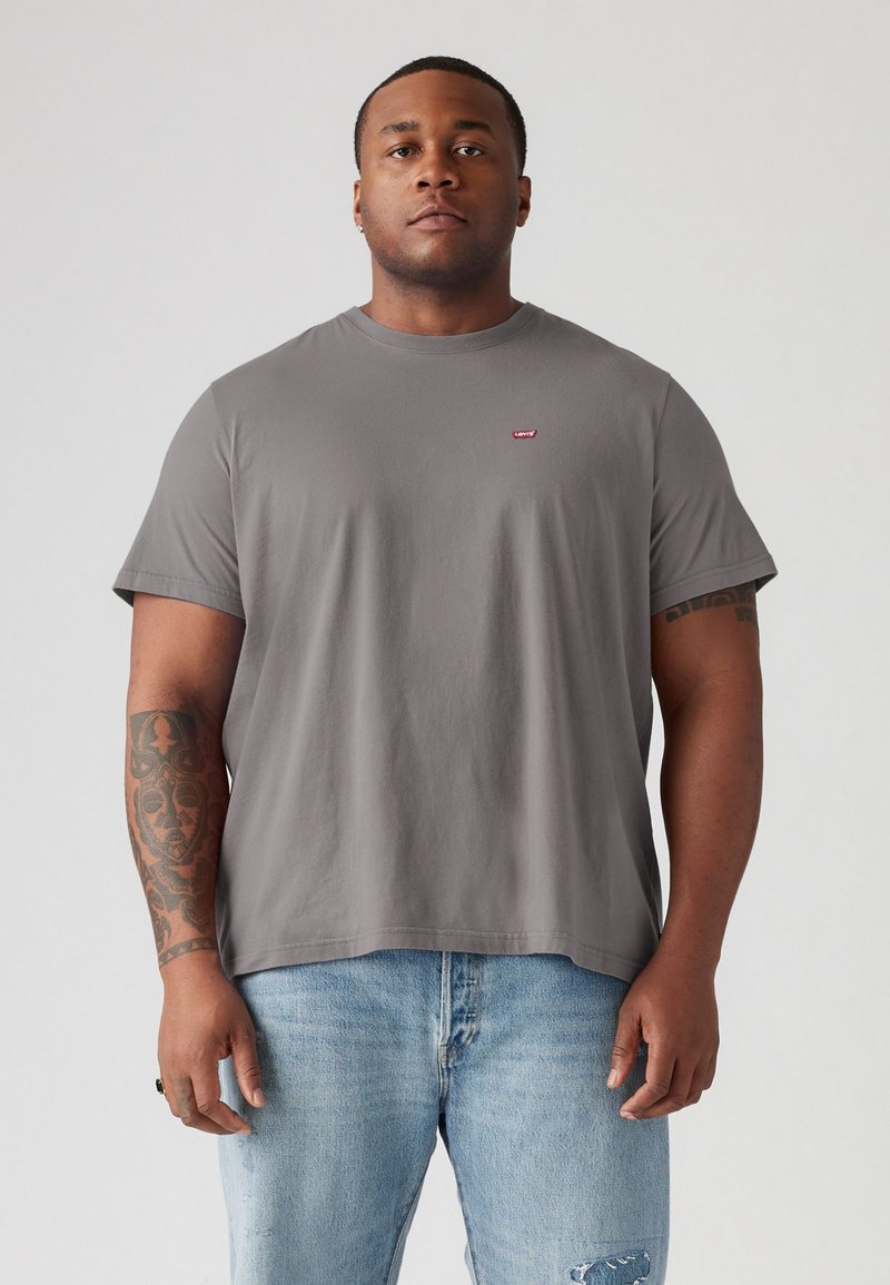 Grijze katoenen t-shirt met een ronde halslijn, korte mouwen en een klein rood logo op de borst. Losse pasvorm en een zachte textuur. G gedragen met lichtblauwe jeans.