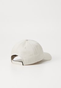 Beige színű pamut baseball sapka kerek koronával és napellenzővel, hátul szövetpántos záródással és szellőzőnyílásokkal.