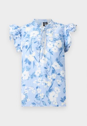 Ανοιχτό μπλε λουλουδάτο μπλουζάκι με λευκά και μπλε λουλούδια, κοντά μανίκια με βολάν και λεπτομέρεια με κορδόνι στο λαιμό σε απλό φόντο.