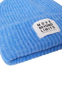 Niebieska dzianinowa czapka z prążkowaną fakturą, z białą metką z napisem "MOVE BEYOND LIMITS" i "FREEDOM STARTS HERE."