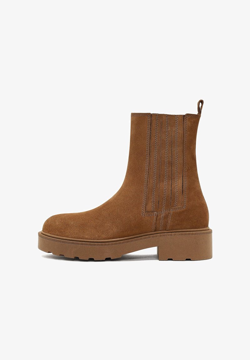 Bottines en daim marron avec une semelle en caoutchouc épaisse, ornées de coutures verticales et d'une languette à l'arrière. Texture lisse.