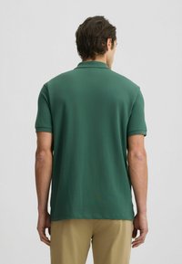 Polo verde a maniche corte realizzato in tessuto morbido, con colletto classico e orlo dritto, indossato con pantaloni beige.