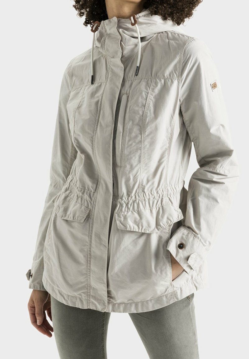Chaqueta gris claro con capucha ajustable, cintura con cordón, dos bolsillos frontales y puños abotonados; textura de tela suave y ligeramente arrugada.