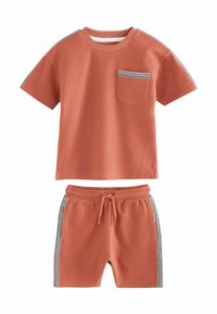 Camiseta de textura de gofre en color óxido, con manga corta y bolsillo en el pecho; combinada con pantalones cortos a juego que presentan rayas laterales y cintura ajustable.