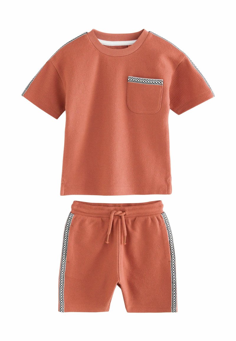 Camiseta de textura de gofre en color óxido, con manga corta y bolsillo en el pecho; combinada con pantalones cortos a juego que presentan rayas laterales y cintura ajustable.