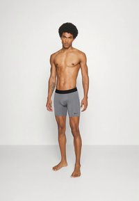 Sive športne kratke hlače s črnim pasom in logotipom, z oprijetim krojem in gladko teksturo, prikazane na stojecem modelu.