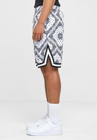 Black and white patterned shorts with a drawstring waistband, featuring side slits and contrast black trim. Worn with white sneakers.