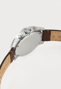 Montre en acier inoxydable argenté avec un bracelet en cuir marron, cadrans chronographe et trois poussoirs sur le côté droit. Dos lisse et plat.