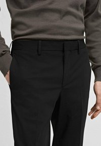 Pantalon noir ajusté, avec des poches latérales et une texture lisse. Assorti avec un pull gris à la taille.