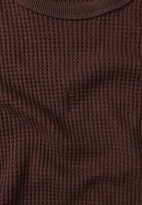 Pull en maille côtelée marron avec un motif texturé, doté d'un col rond et d'un petit logo brodé au centre.