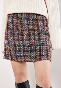 Gonna mini in tweed nera con fili multicolore. Presenta una vestibilità strutturata, una trama testurizzata e un orlo dritto. Abbinata a un maglione crema.