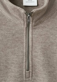Maglione in maglia a coste beige con una mezza zip in argento e un'etichetta di dimensione che indica Regular EUR-USA M MEX M.