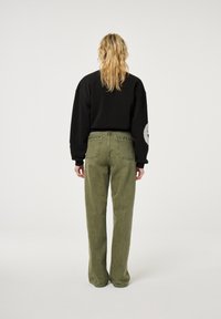 Zwarte cropped sweatshirt met oversized mouwen, gecombineerd met olijfgroene wijde jeans met zichtbare naden en achterzakken.