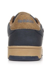 Vista posteriore di una sneaker blu navy con un tallone in suede beige, caratterizzata da "Redskins" impresso sul tallone e una suola in gomma beige chiaro.