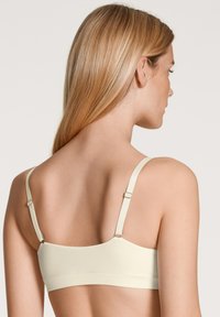 Lichtroomkleurige bh met een naadloos ontwerp, verstelbare bandjes en zacht materiaal. Gladde textuur met subtiele hardwaredetails.