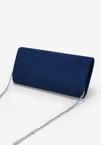 Bolso de mano de ante sintético azul marino con forma rectangular, cadena plateada y detalles de costura decorativa a lo largo del borde superior.