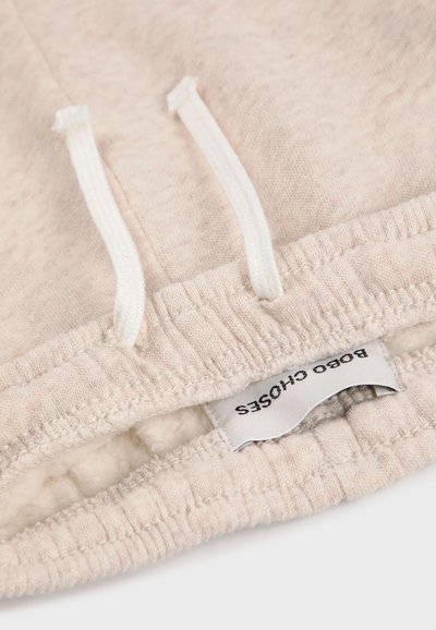Hellbeige Stoff mit einer weichen Textur, elastischem Bund mit Kordelzügen und einem Etikett, auf dem "Bobo Choses" steht.