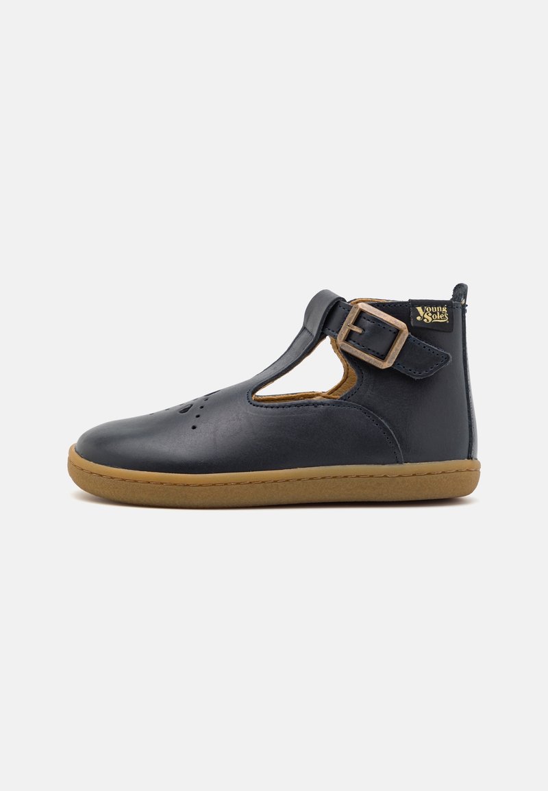 Chaussure enfant en cuir bleu marine avec bride en T, fermeture à boucle, bout perforé et semelle en caoutchouc beige, avec l’étiquette "Young Soles" au talon.