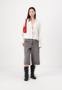Hvitstripete bluse med frontknute, grå vide cropped bukser, og svarte overknebøtter. Legger til en rød crossover-veske for kontrast.