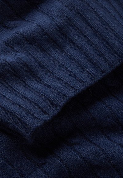 Navy blue knitted fabric with textured ribbed pattern, soft and slightly fuzzy finish, flowing drapes highlighting the material's flexibility.