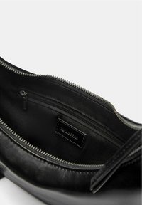 Fekete kézitáska texturált külsővel, cipzáras záródással és textillel bélelt belsővel, amely egy kis cipzáras zsebet és márkajelzést tartalmaz.