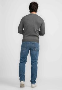 Grijze trui met een ronde hals, gecombineerd met lichtblauwe jeans en witte sneakers, gezien vanuit de achterkant tegen een witte achtergrond.
