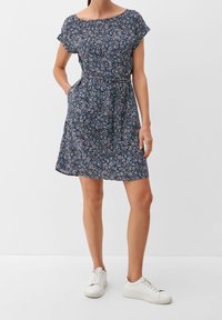 Marinblå klänning med blommönster, korta ärmar, smal midja och fickor; i kombination med vita sneakers. Mjuk tygkvalitet, avslappnad design.