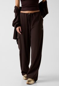 Bruine, lichte, loszittende broek met een elastische tailleband met trekkoord, zijzakken en een logodetail aan de voorkant.