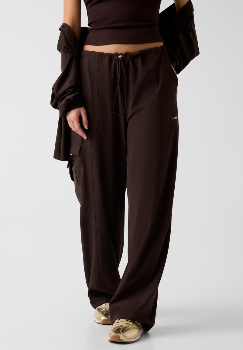 Bruine, lichte, loszittende broek met een elastische tailleband met trekkoord, zijzakken en een logodetail aan de voorkant.