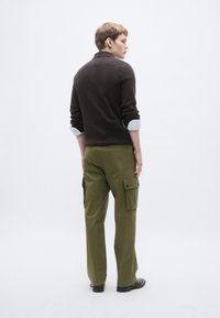 Brūns džemperis ar augstu apkakli un uzlocītām aprocēm, kombineēts ar olīvu zaļu kravas biksēm ar sānu kabatām un taisnu bikšu kāju dizainu.