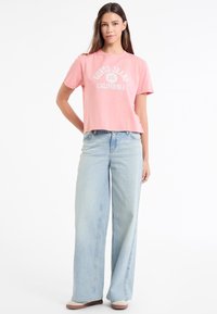 Roosa lühike t-särk, millel on graafika 'GUESS JEANS CALIFORNIA', kombinatsioonis helesiniste laia säärega teksadega. Lihtne disain lühikeste varrukatega.
