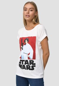 Hvid bomulds T-shirt med et grafisk print af en karakter i en hvid robe og en sort laservåben, med fed tekst "STAR WARS" i sort.