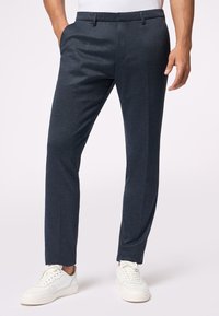 Schlanke, dunkelblaue Hose aus strukturiertem Stoff, mit Fronttaschen und flachem Design, kombiniert mit weißen Sneakers.