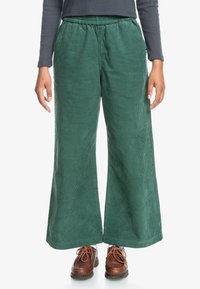 Green corduroy wide-leg pants with a textured surface and an elastic waistband, paired with brown lace-up shoes.
