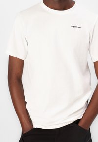 Biała bawełniana koszulka z krótkim rękawem, z okrągłym dekoltem, z małym czarnym logo G-Star Raw na lewej części klatki piersiowej.