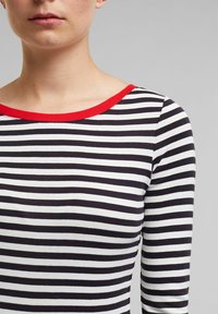 Schwarz-weißer gestreifter Oberteil mit runder Ausschnitt, ausgestattet mit rotem Rand. Der Stoff wirkt weich und sitzt enganliegend mit langen Ärmeln.