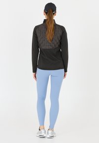 Schwarze Sportjacke mit strukturiertem Rücken, kombiniert mit hellblauen Leggings und silbernen Sneakers. Entworfen für aktive Kleidung mit modernem Schnitt.