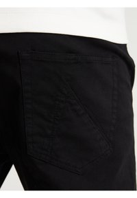 Zwarte broek met een opvallende ruitvormige achterzak, gemaakt van textuurstof met zichtbare stiksels.