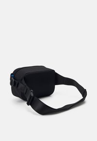 Kompakt svart midjeväska med mesh-fickor fram, justerbar rem och plastspänne på vit bakgrund.