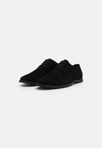 Nelle scarpe derby nere in suede, con una texture liscia, la punta appuntita e un design tradizionale con lacci. Suola piatta con minimo battistrada.