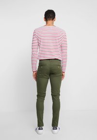 Grüne Slim-Fit-Hose aus Baumwolle, kombiniert mit einem rot-weiß gestreiften Langarmshirt. Gestylt mit weißen Sneakers.