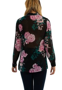 Donna che indossa una camicia nera trasparente con motivi floreali rosa e jeans scuri, mostrata di spalle su uno sfondo bianco.