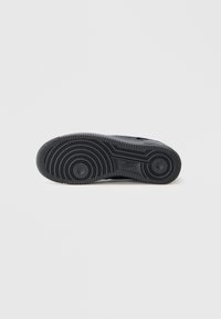 Semelle de sneaker noire en caoutchouc avec des motifs circulaires et des stries. Présente un design texturé et un logo de marque en relief.