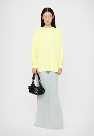 Neon yellow long-sleeve top paired with a light blue denim skirt; model holds a black bag with decorative studs and straps.