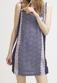 Námořnické modré bezramínkové šaty s vlnkovým vzorem v světle modré a krémové barvě, s postranními panely a logem Adidas na hrudi.