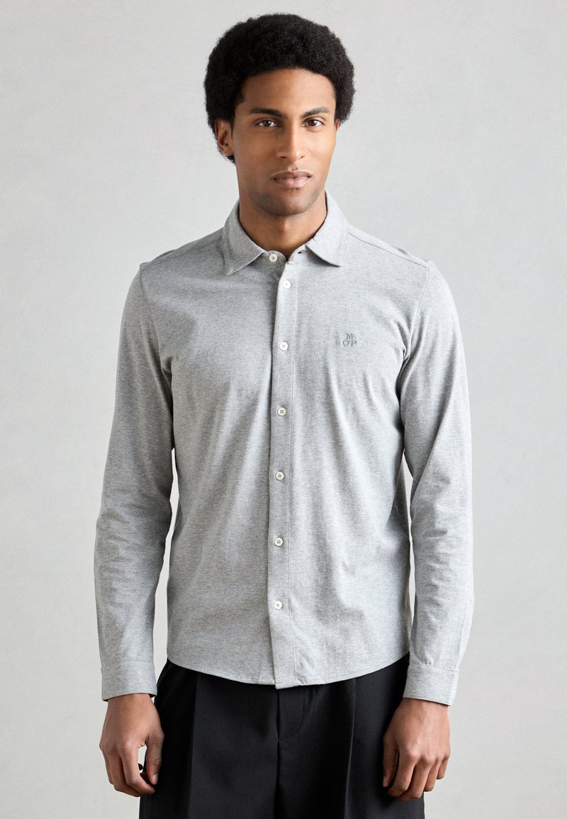 Camisola cinzenta de manga comprida feita de mistura de algodão, com abotoamento frontal, gola e logo discreto no peito. Textura suave e design ajustado.