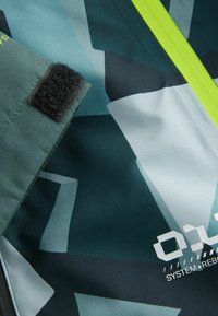 Viacfarebná tkanina s abstraktnými geometrickými vzormi v odtieňoch zelenej a čiernej, s neonovo zeleným akcentom a detailom na suchý zips.
